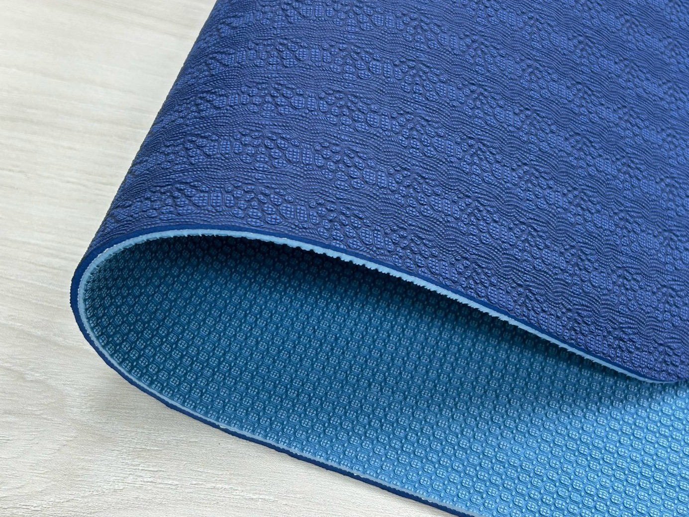 TPE Yoga Mat Top vs Bottom Surface Texture Detail Close-up of folded TPE yoga mat corner showing embossed top surface texture versus smoother textured underside
